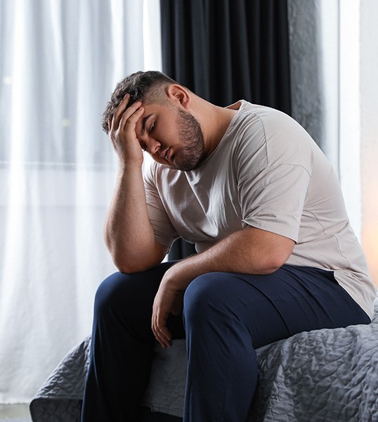 a tired man sitting on his bed